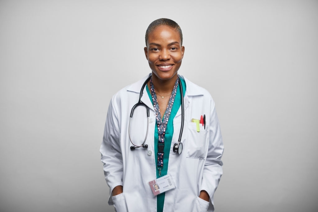 Portrait of confident smiling doctor with stethoscope. Female healthcare worker is standing with hands in pockets. She is against white background